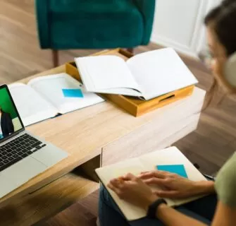 Pessoa estudando em casa com notebook e materiais didáticos em uma mesa organizada